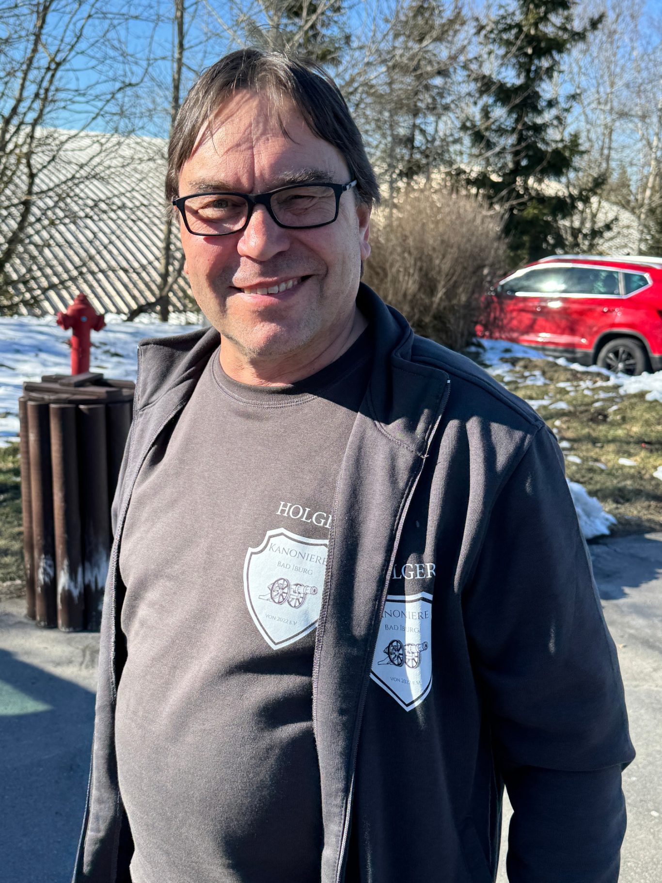 Holger Niemüller Mann mit Brille und grauem Shirt, lächelt vor verschneiter Landschaft.