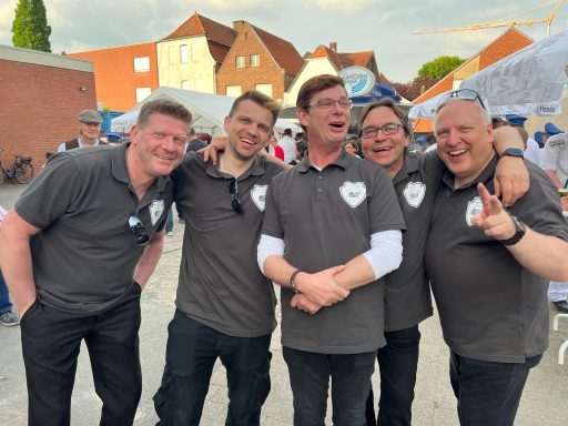 Fünf Männer in grauen T-Shirts stehen lachend zusammen.