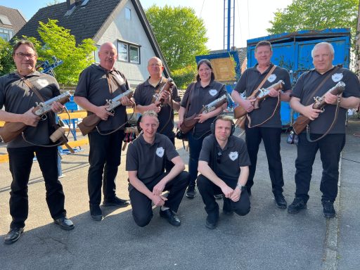 Gruppe von acht Personen in schwarzen Shirts, die Musikinstrumente halten.