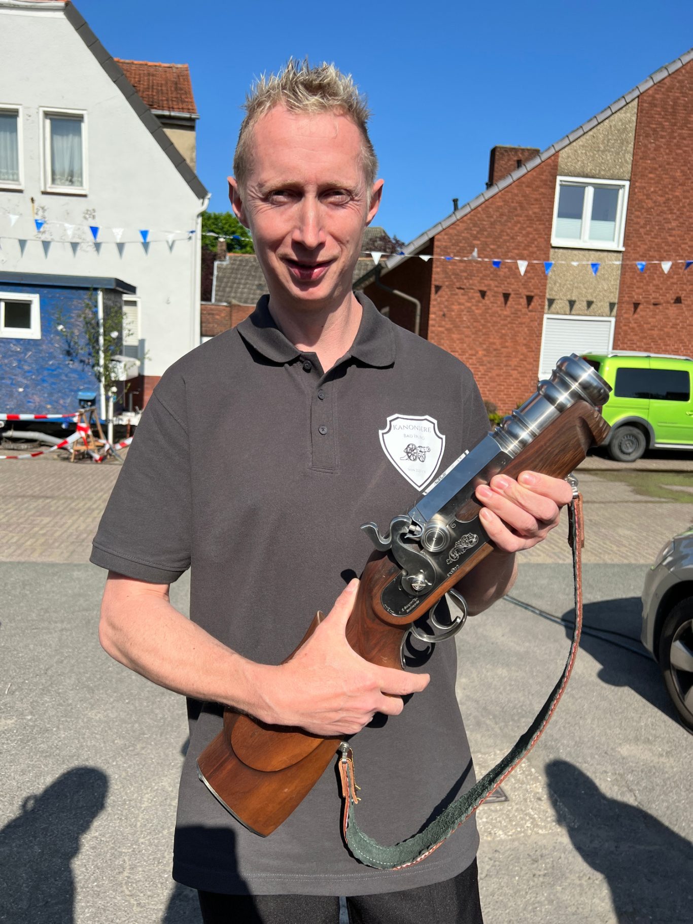 Silvio Motzkus Mann hält ein Gewehr mit Holzgriff, steht vor einer ländlichen Kulisse.