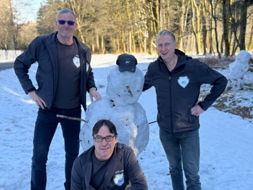 Drei Männer posieren mit einem Schneemann im Schnee.