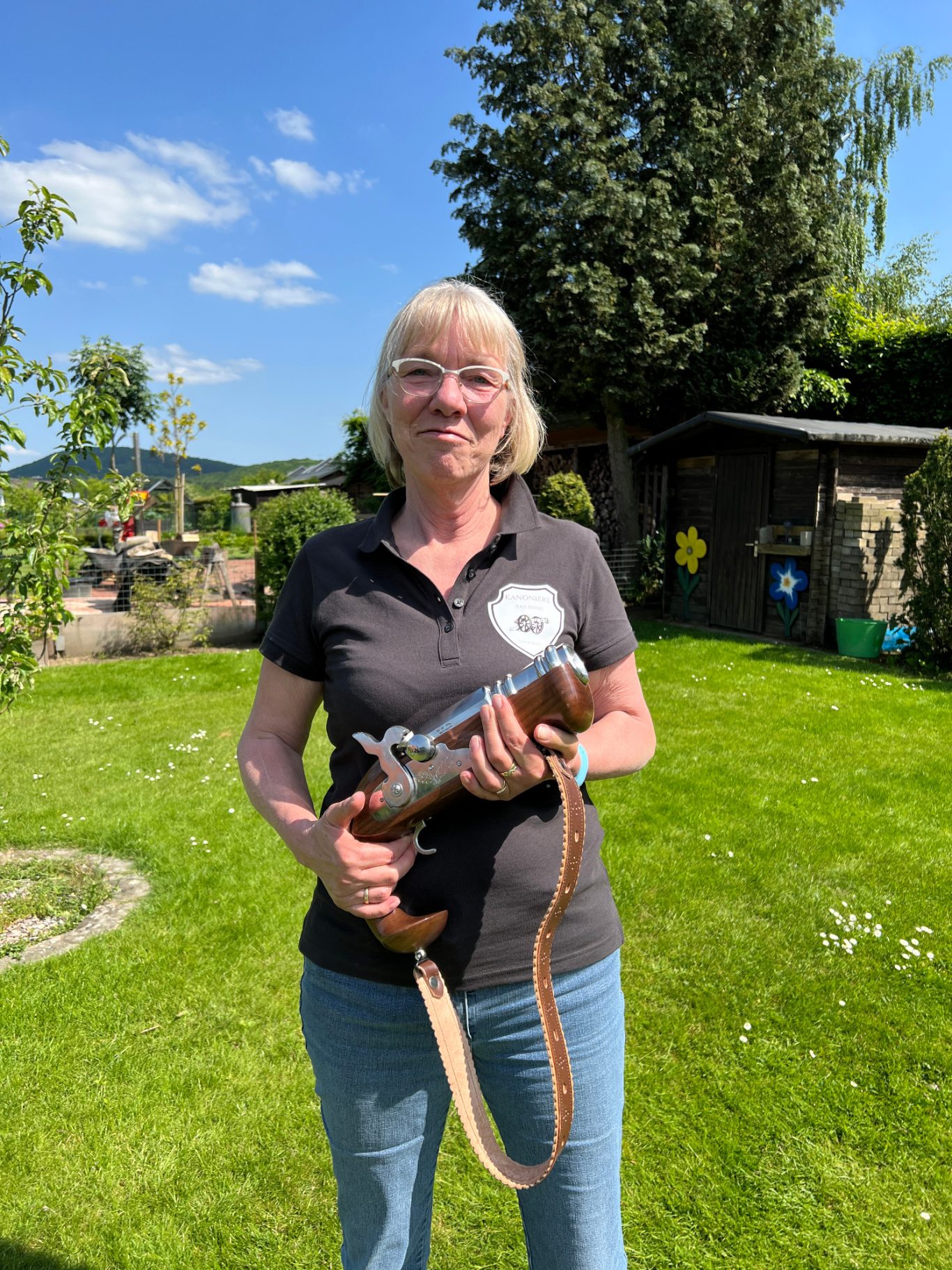 Dagmar Streuter Frau mit kurzer blonder Frisur hält eine Holzpfeife in einem grünen Garten.