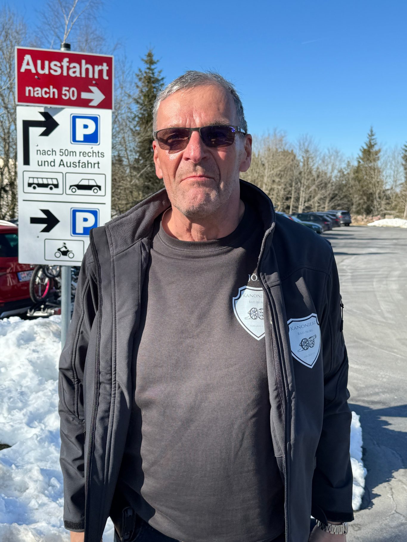Jörg Haverkamp Mann mit Sonnenbrille und grauem T-Shirt steht vor einem Parkplatzschild im Schnee.