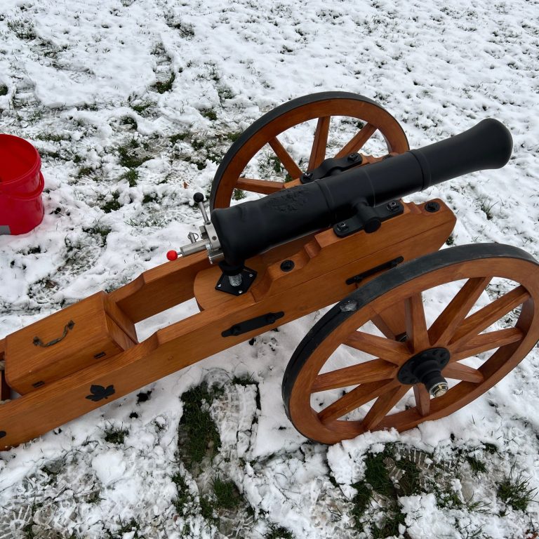 Holzkanone mit großen Rädern auf schneebedecktem Boden.