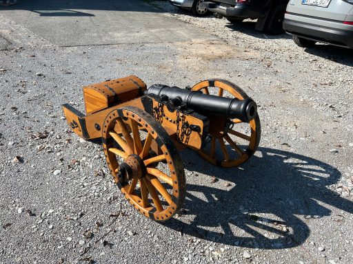 Historische Kanone auf Rädern, aus Holz mit einem schwarzen Geschützrohr.