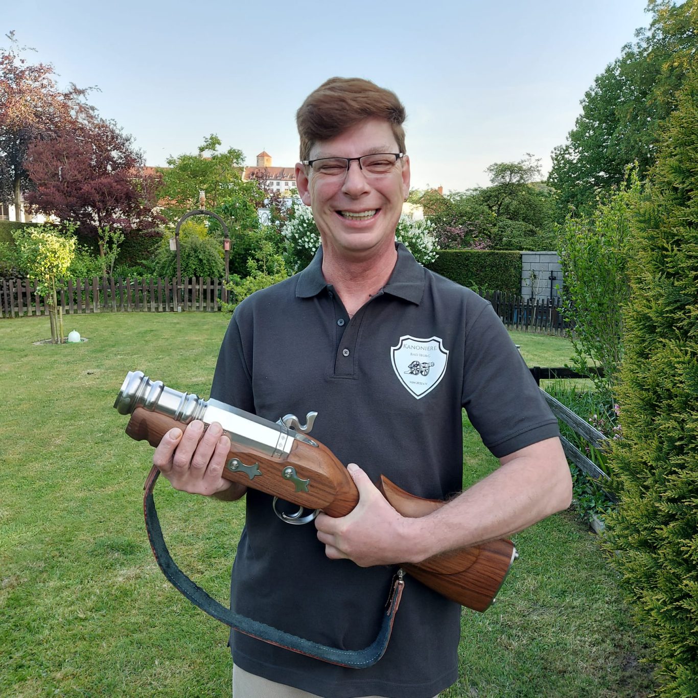 Roland Greiwe Mann im Garten hält ein futuristisches Gewehr mit Holzgriff und lächelt.