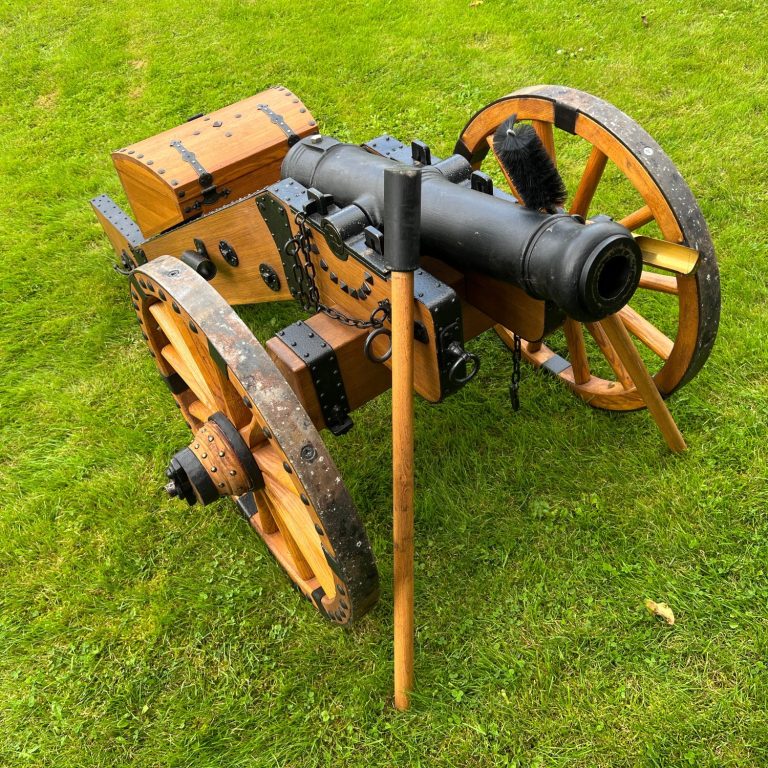 Holzkanone auf Rädern, mit einem schwarzen Lauf und einem Holzständer auf grünem Gras.