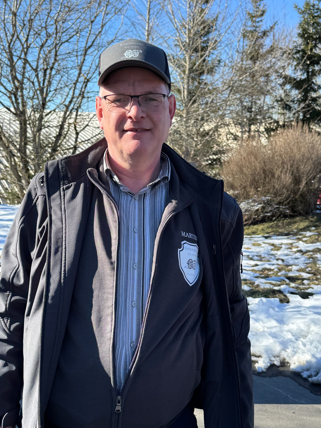 Martin Streuter Mann im Freien, trägt eine Kappe und eine Jacke, mit schneebedecktem Boden und Bäumen im Hintergrund.