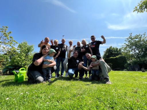 Gruppe von Menschen auf einer Wiese, einige winken, strahlendes Wetter.